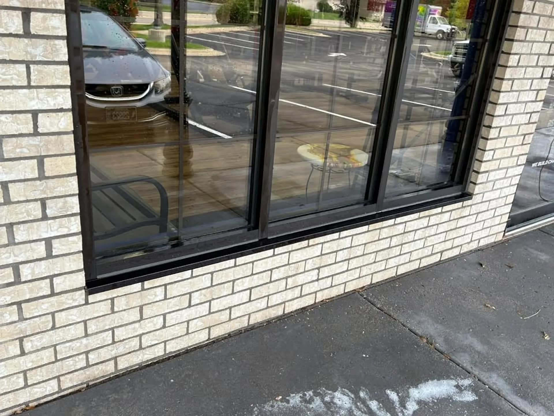 Storefront glass washed clear, parking lot reflected in the pane