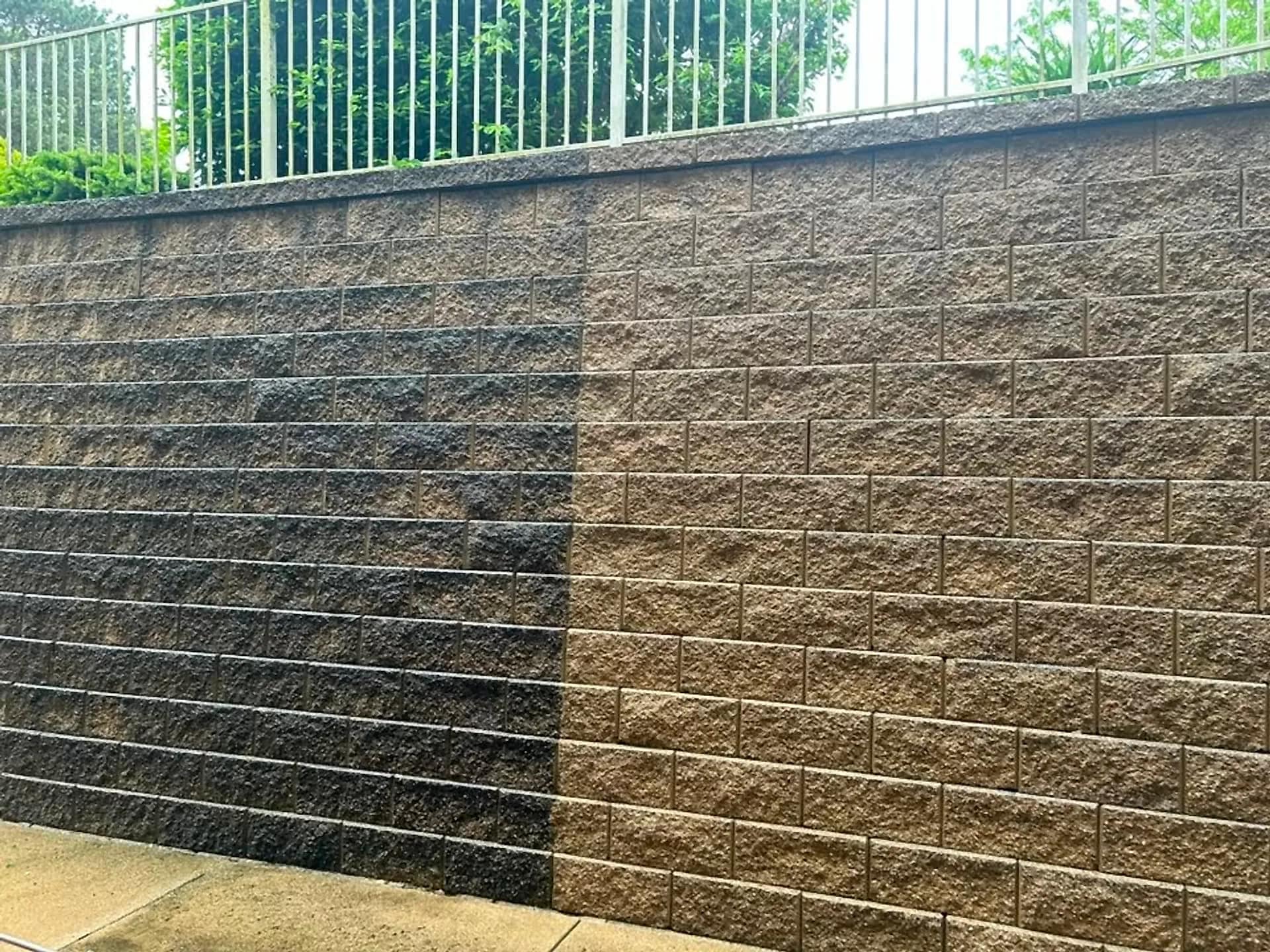 Block retaining wall half washed, dark algae on one side and original stone colour on the other