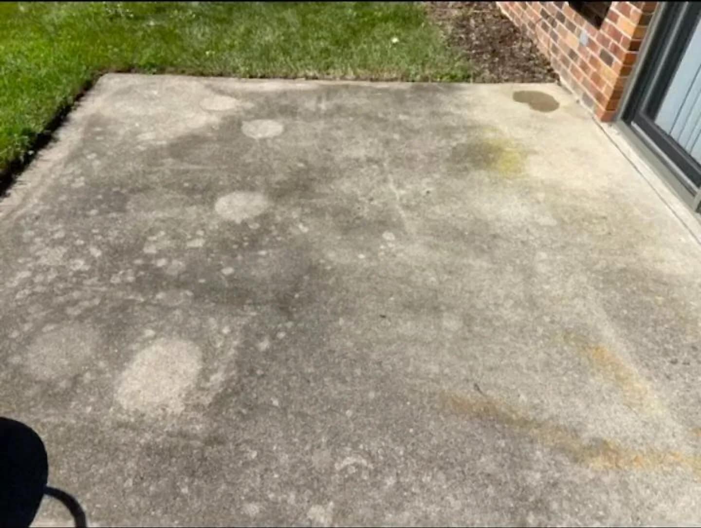 Concrete patio mottled with algae staining before a surface-cleaner pass